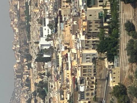       Dense hillside view of tan–colored buildings making up the old medina district of a Moroccan city under hazy midday light.
  