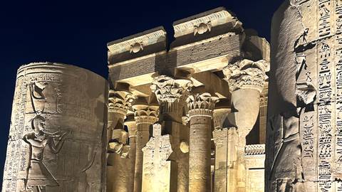       Night view of illuminated stone columns and reliefs of Kom Ombo Temple.
  