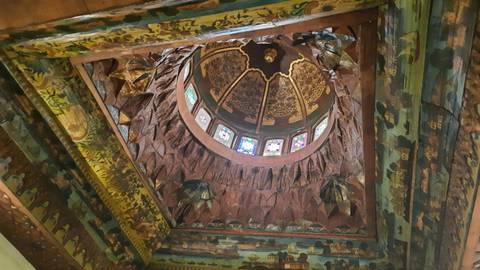       Intricately painted and carved domed ceiling with colorful stained-glass windows viewed from below.
  