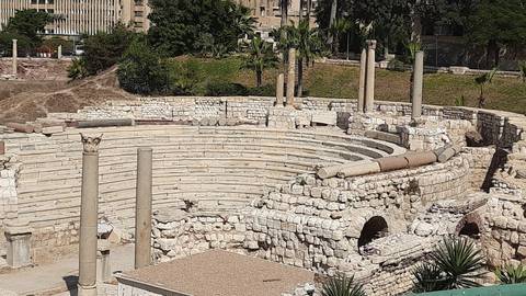       Stone Roman-era amphitheatre ruins with broken columns under bright sun.
  