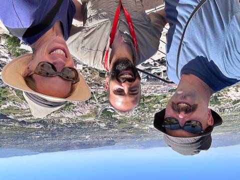       Smiling trio takes a selfie with expansive Cappadocia rock formations and villages in the background.
  