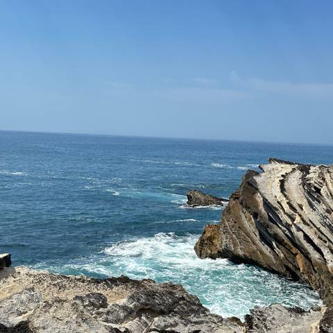       Jagged sea cliff jutting into the blue Atlantic with calm horizon beyond.
  
