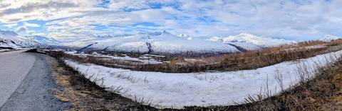       Expansive snowy valley and distant peaks under a patchy blue sky in late spring.
  