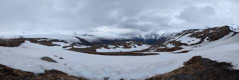       High alpine pass still covered in lingering winter snow beneath dramatic grey skies.
  