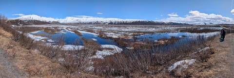       Vast tundra wetlands dotted with melting snow pools stretching toward a distant white mountain wall.
  
