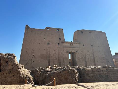       The massive sandstone pylons of Edfu Temple rise under a flawless blue Egyptian sky.
  