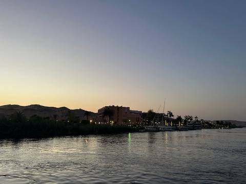       Soft evening light settles over riverside buildings and palm trees along the Nile.
  