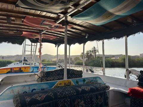       The interior of a shaded boat on the Nile at golden hour with desert hills in the background.
  