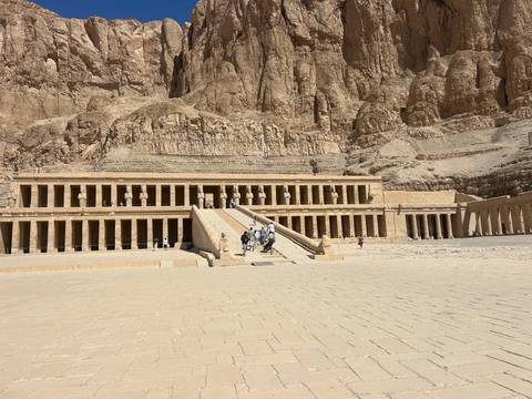       The grand terraced facade of Hatshepsut Temple rises against sheer desert cliffs under a bright sky.
  