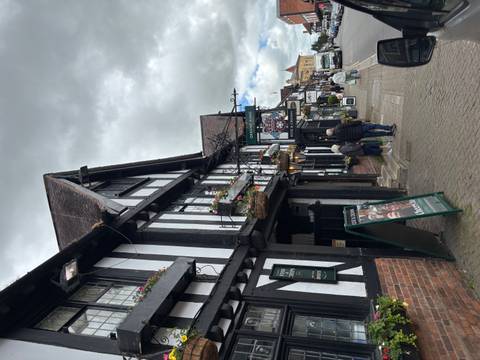       Historic black-and-white timbered pub frontage with hanging baskets on a narrow village street.
  