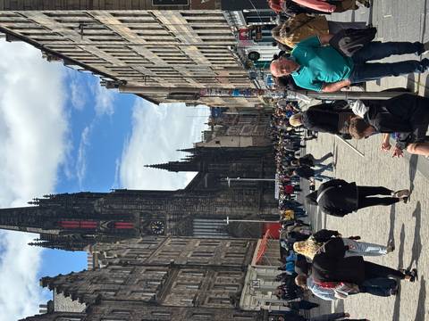       Bustling Royal Mile in Edinburgh with crowds and the tall spire of The Hub rising above historic stone buildings.
  