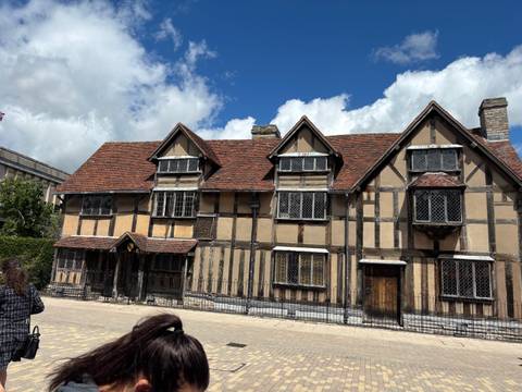       Timber-framed Shakespeare’s Birthplace house under a bright sky with a visitor in the foreground.
  