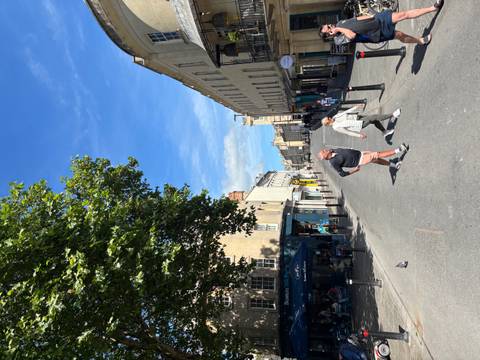       Sunny pedestrian street in Bath with blue sky, historic facades and two people crossing the road.
  