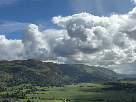       Dramatic green mountain ridge and valley under towering cumulus clouds.
  
