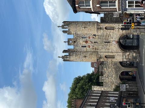       Stone medieval gatehouse with towers and heraldic shields set against a blue sky.
  