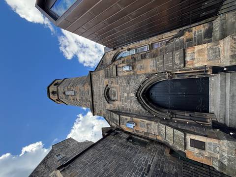      Upward perspective of a tall stone church tower framed by blue sky and scattered clouds.
  