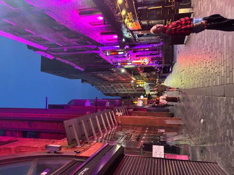       Vibrant neon-lit pedestrian street at dusk with colorful façades and nightlife atmosphere.
  