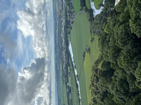      Elevated view of green fields, winding river and distant coast under layered clouds.
  