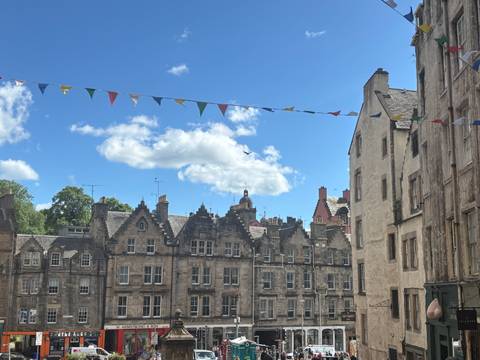       Row of sandstone tenements with festive bunting strung across a clear blue sky.
  