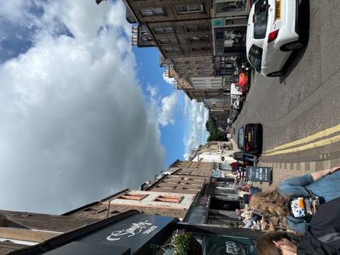      Lively town street with cafes, cars and shoppers beneath a large patch of dark cloud.
  