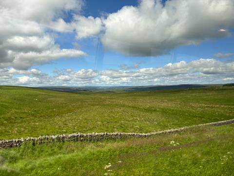      Wide grass-covered uplands and stone field walls stretching into a hazy horizon under fair-weather clouds.
  