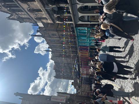       Crowds walking along Edinburgh’s colorful Victoria Street adorned with bunting under bright sunlight.
  
