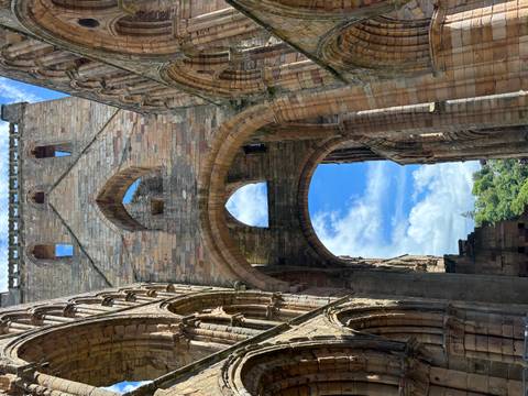       Soaring stone arches of a ruined abbey framing bright blue sky and distant greenery.
  