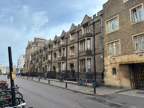       Row of historic stone college buildings with bicycles parked along a quiet Cambridge street.
  