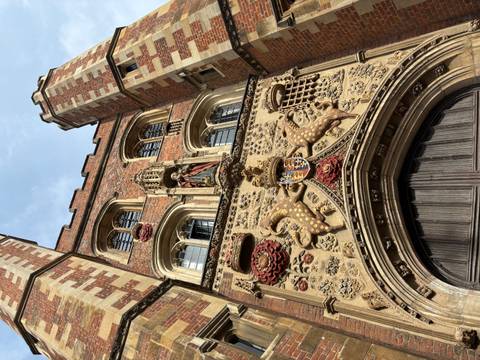       Close-up of Tudor brick gateway adorned with royal coat of arms and carved roses.
  