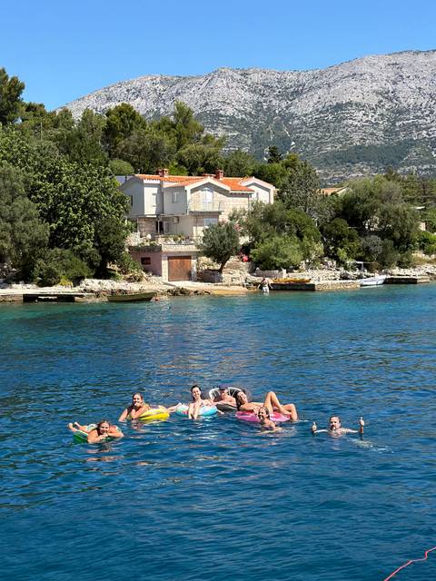       Small group floating on an inflatable raft in turquoise coastal water near stone houses.
  