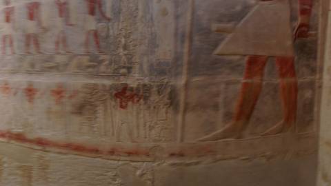       Blurred interior wall showing faint Egyptian reliefs and faded pigment.
  