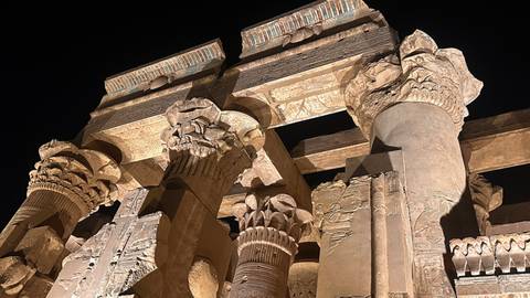       Illuminated sandstone columns and hieroglyphs of Kom Ombo Temple at night.
  