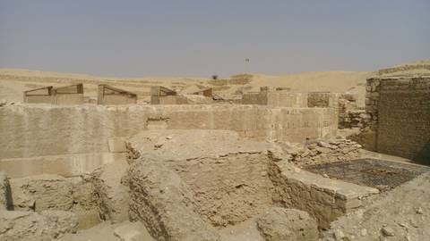      Sandy archaeological excavation of ancient settlement ruins amid barren desert landscape under hazy sky.
  