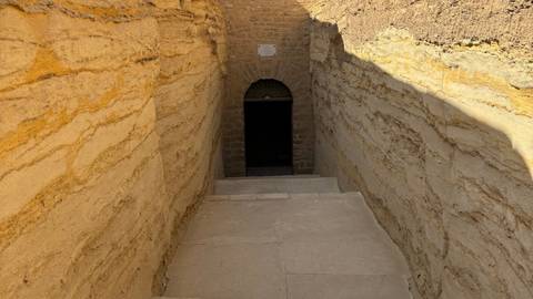       Stone stairway descending between sandstone walls into a dark tomb entrance at Saqqara.
  