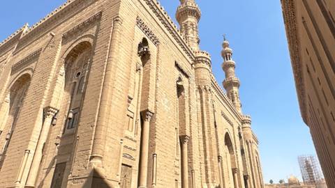       Sandstone mosque with towering minarets and ornate arches set against a clear blue sky
  