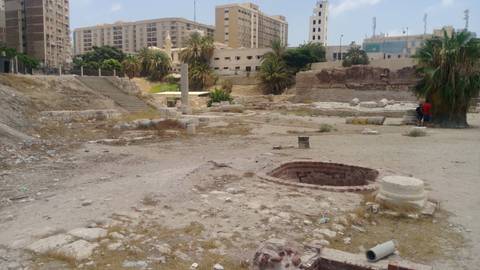       Urban excavation site littered with stones and debris, high-rise apartments in the background
  