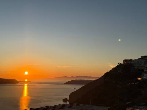       Vibrant sunset over the Santorini caldera with silhouettes of distant islands and calm sea
  