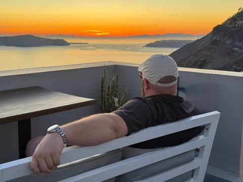       Man relaxing on a terrace bench watching the colorful Santorini sunset over the caldera
  