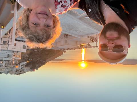       Selfie of two travelers with Santorini sunset and white rooftops behind them
  