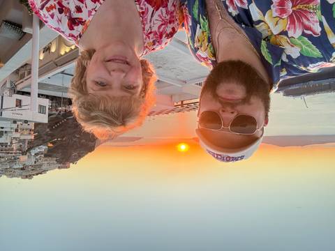       Couple taking a selfie at sunset overlooking Santorini’s caldera and a docked cruise ship
  
