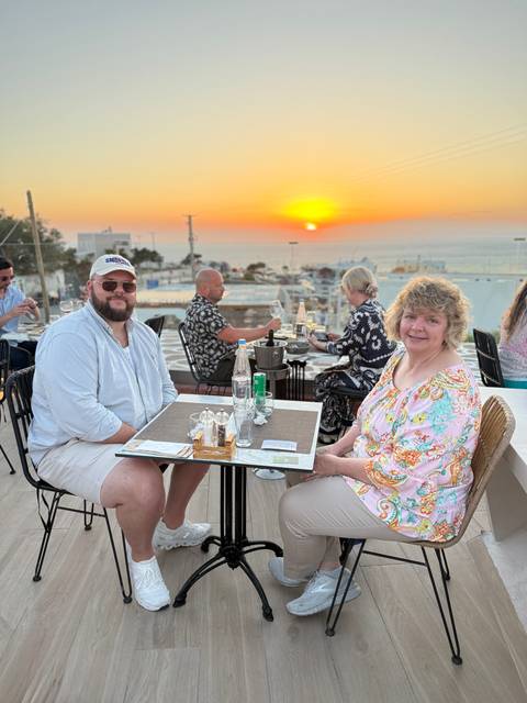       Outdoor restaurant scene at sunset with diners enjoying food and sea views
  