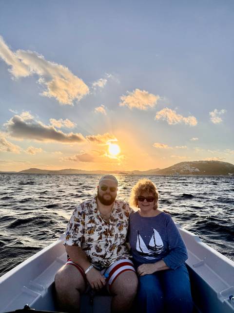       Couple posing on a boat with golden sunset over rolling hills and open sea
  