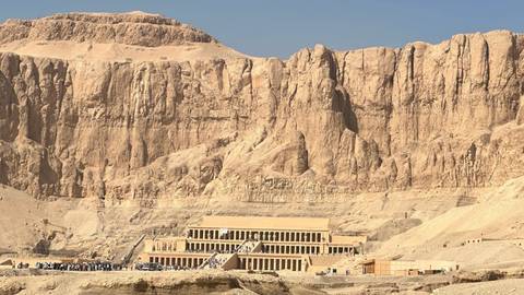       The terraced Temple of Hatshepsut nestled against towering cliffs in the Egyptian desert under clear skies.
  