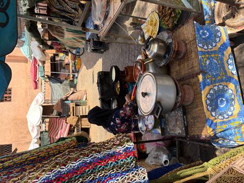      Covered market stall in Morocco with pots and pans cooking traditional street food while a veiled vendor tends to them.
  