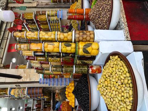       Vibrant display of olives and preserved vegetables stacked in jars at a Moroccan souk.
  
