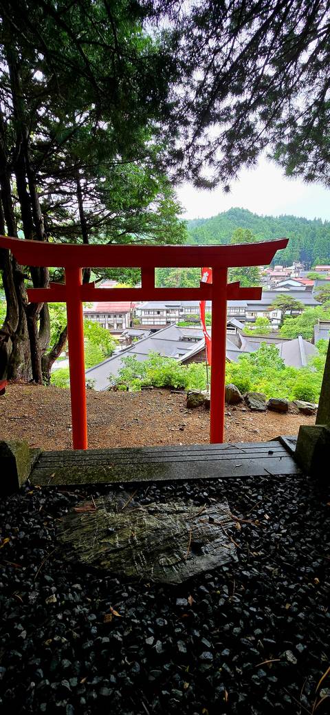       Hilltop view of town rooftops framed by bright red torii posts
  