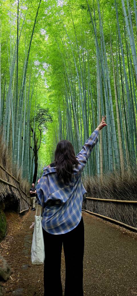       Back view of woman raising a peace sign amid towering green bamboo stalks
  