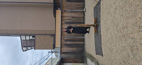       Single participant in robe standing beside wooden sword-cutting stand in gravel yard
  