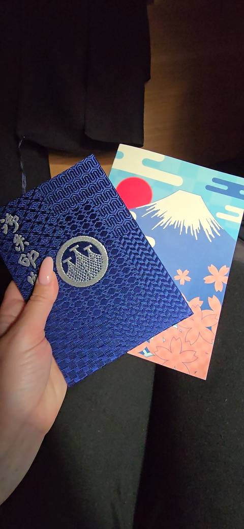       Hand holding an ornate blue travel stamp book beside colorful Mount Fuji artwork
  