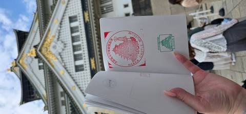       Open passport book showing Osaka Castle stamps held before the blurred castle facade
  